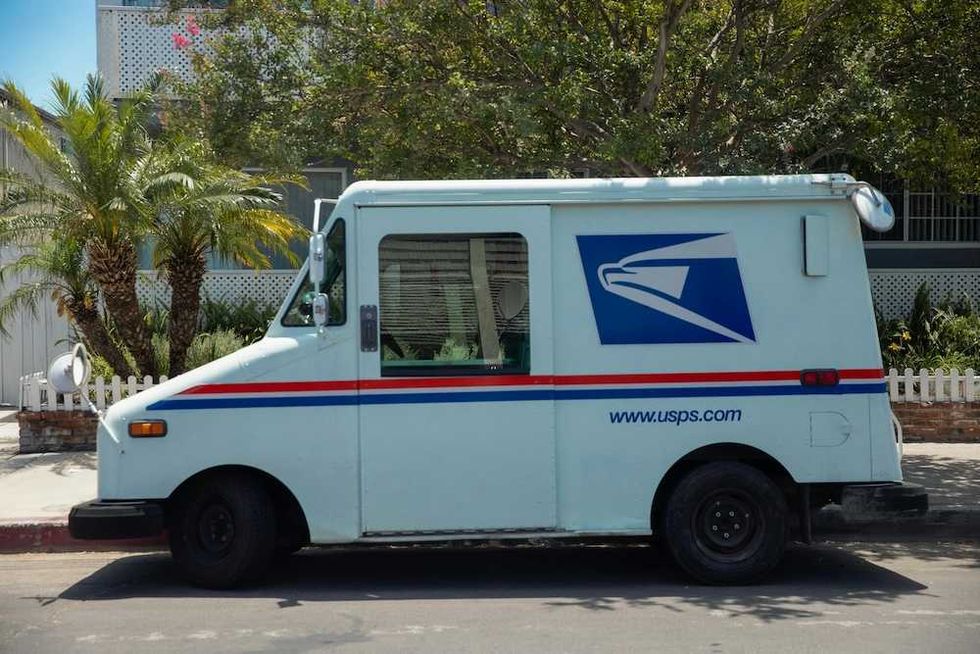 USPS mail truck parked on a street with trees in the background.