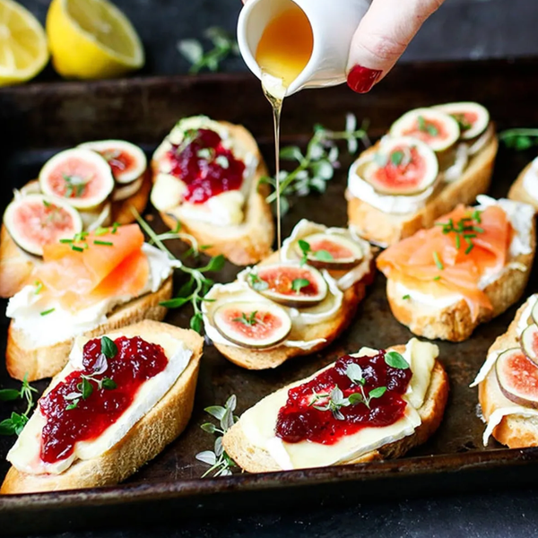 Various bruschetta with figs, salmon, and jam, drizzled with honey on a rustic tray.