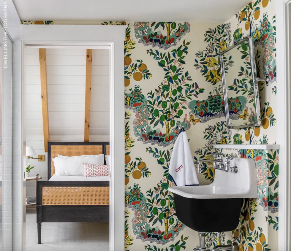 Vibrant bathroom wallpaper; view into a bedroom with wood beams and a wicker bed.