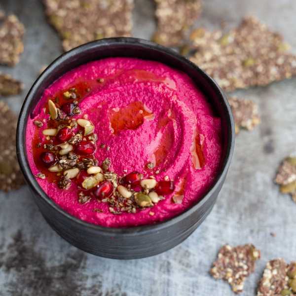 Vibrant beet hummus in a black bowl, garnished with seeds and pomegranate arils.