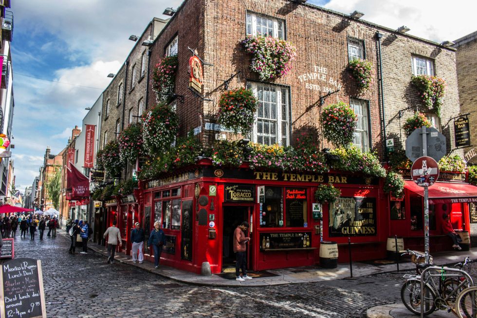 Vibrant red corner pub with flower displays on cobblestone street, lively atmosphere.