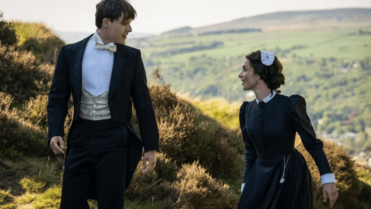 Victorian-era couple walking on a grassy hill in formal attire, sharing a smile.