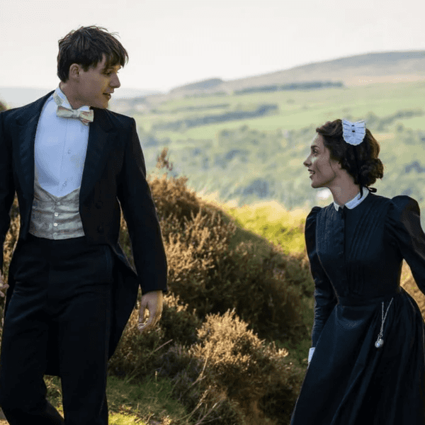 Victorian-era couple walking on a grassy hill in formal attire, sharing a smile.
