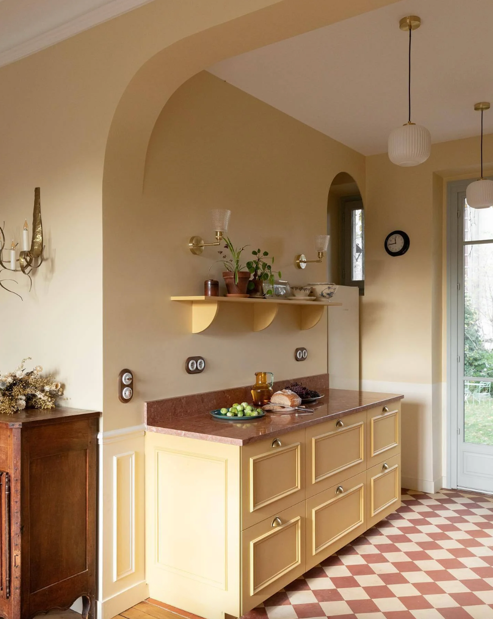 Vintage kitchen with yellow cabinets, red countertop, potted plant, and checkered floor.