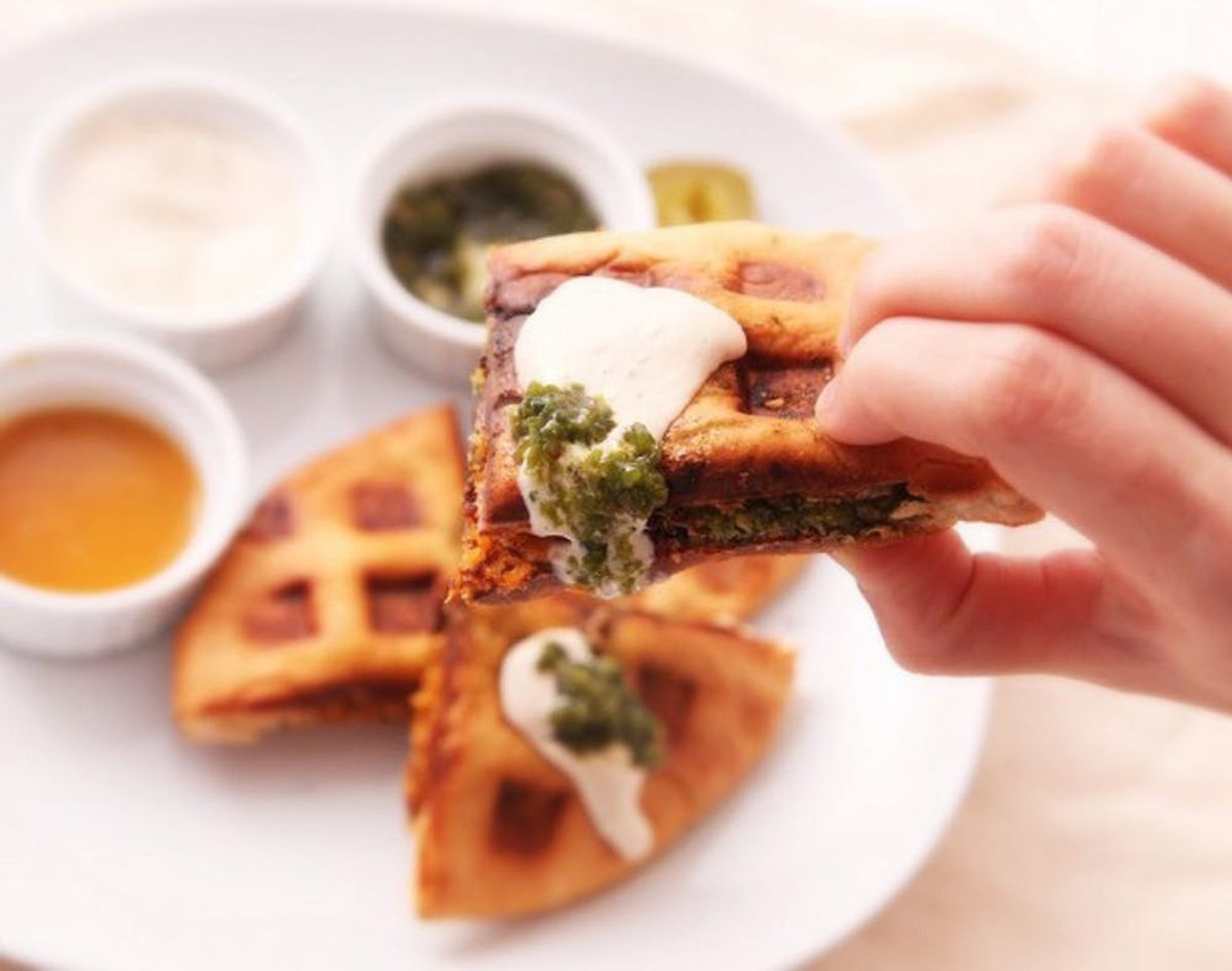 Waffle Iron falafel waffles held in a hand with a white plate and ramekins of sauce make one of 25 easy college meals