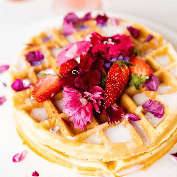 Waffle topped with strawberries and vibrant pink edible flowers.