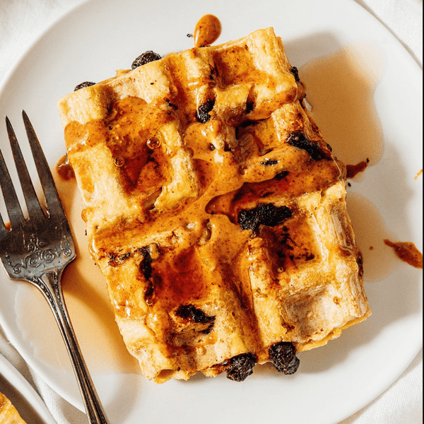Waffle with chocolate chips and syrup on a white plate beside a fork.