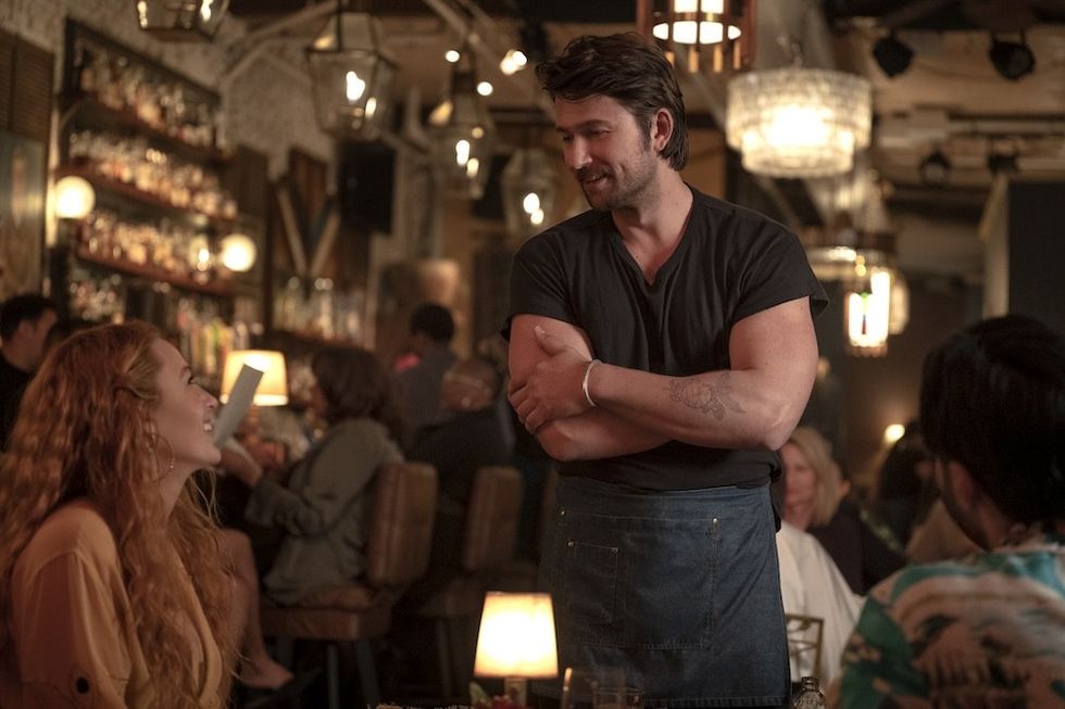 Waiter talking to a smiling woman in a dimly lit restaurant.
