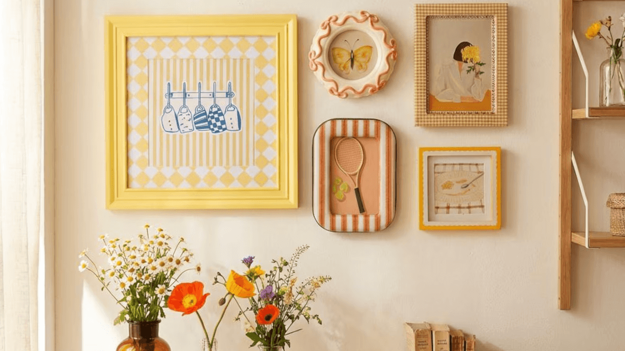 Wall with colorful framed art, flowers in vases, books, and folded towels on a wooden shelf.