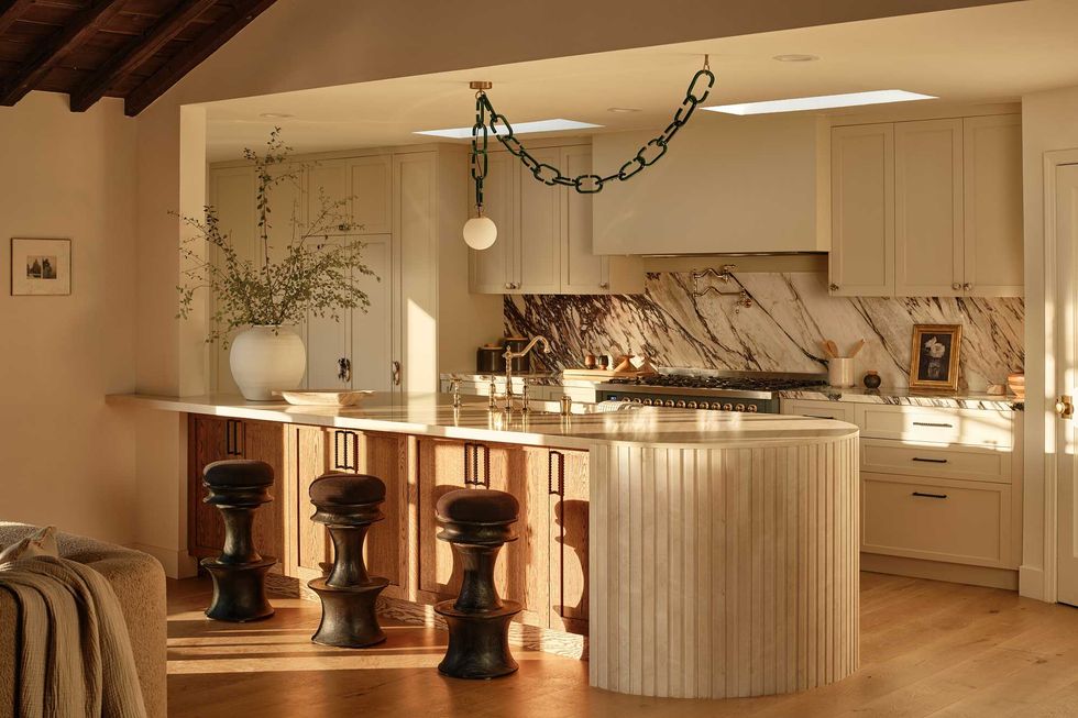 Warm, inviting kitchen with marble backsplash and three bar stools at a curved island.
