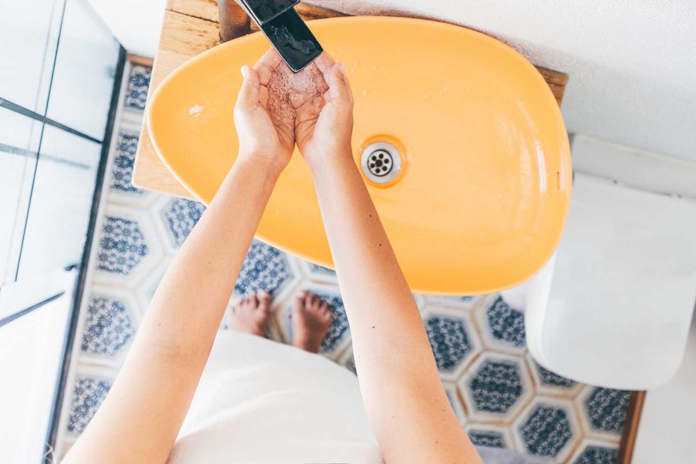 Washing hands under a black faucet in a yellow basin, over patterned floor tiles.
