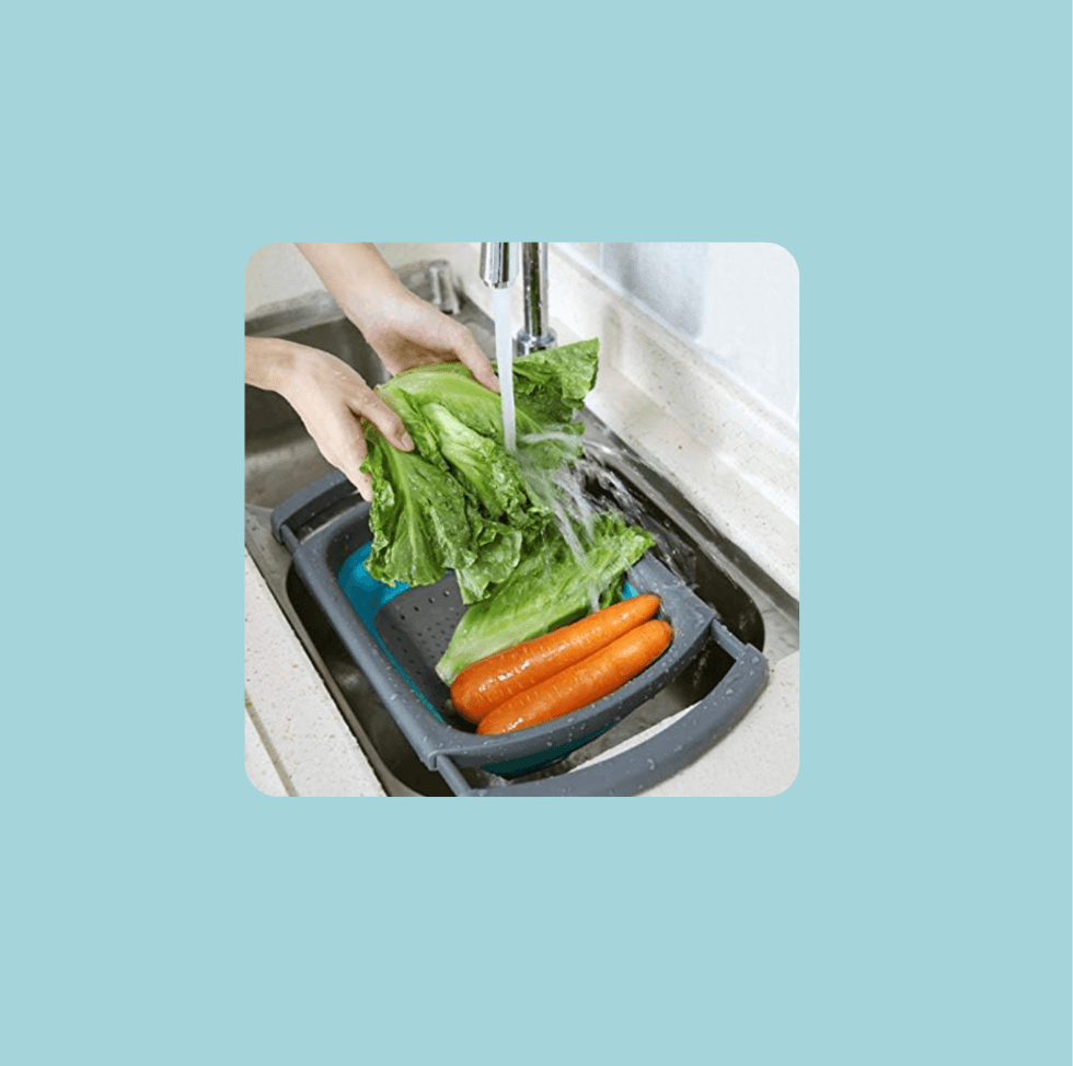 Washing lettuce and carrots in a colander under running water in a kitchen sink.