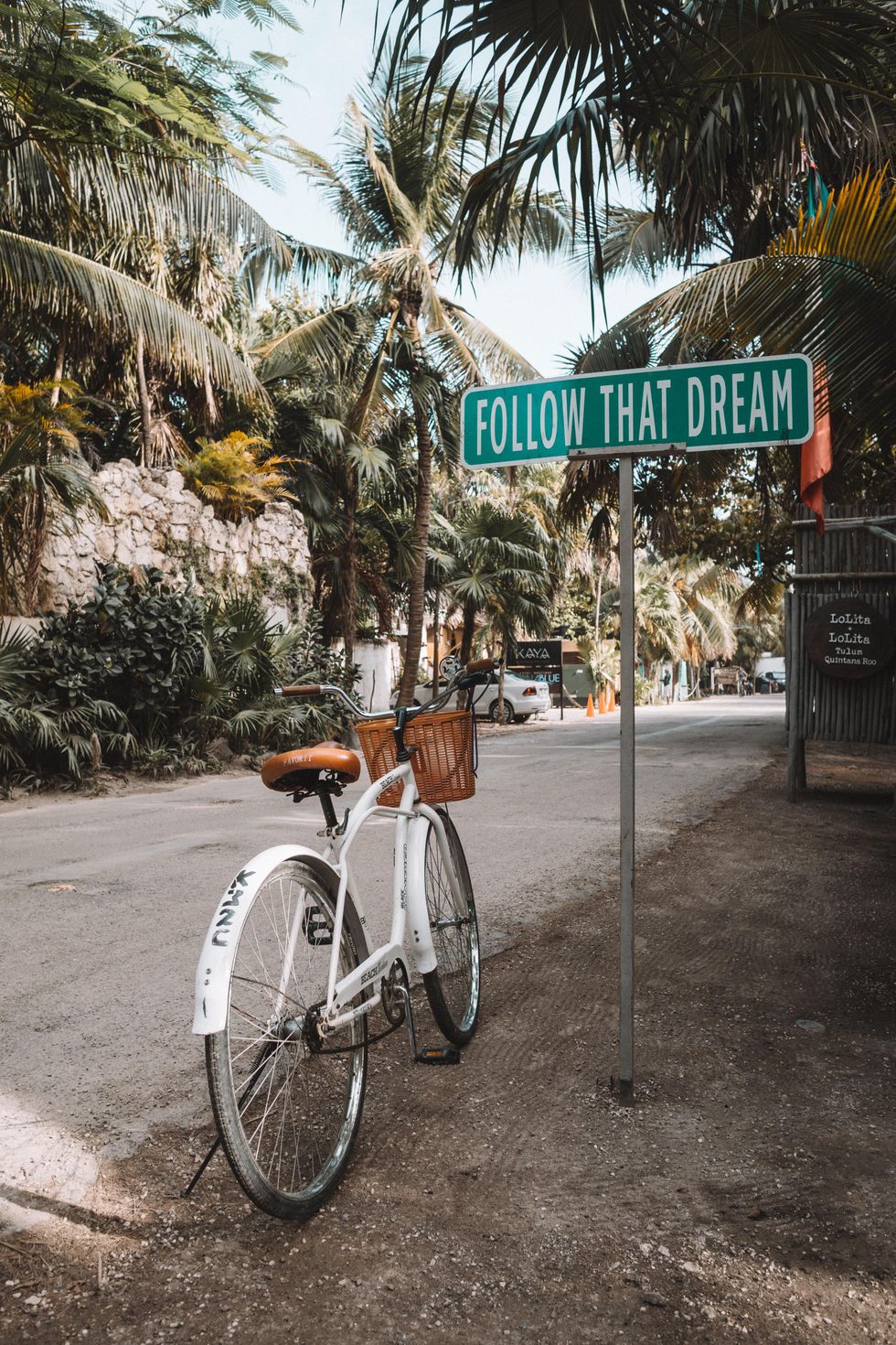 white bike with brown basket on side of road in Tulum