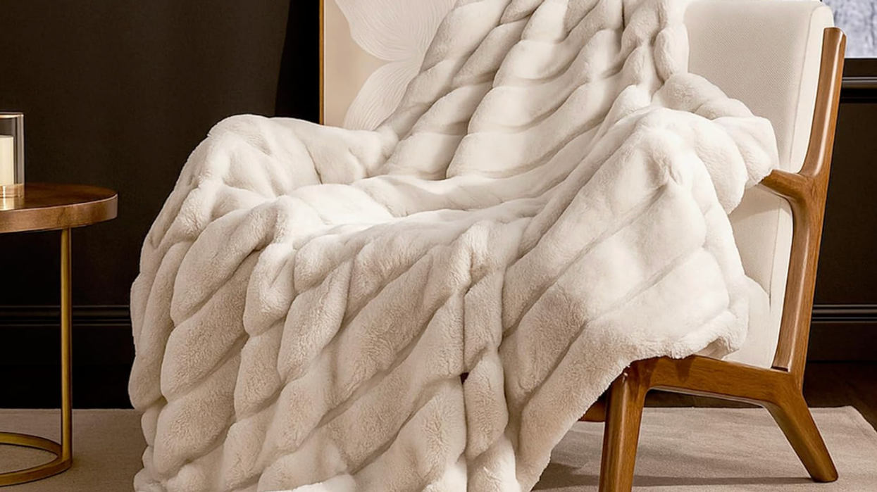 White faux fur throw draped over a modern armchair near a window and side table.