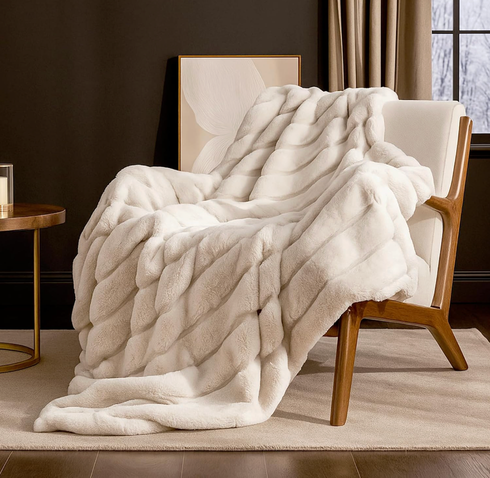 White faux fur throw draped over a modern armchair near a window and side table.