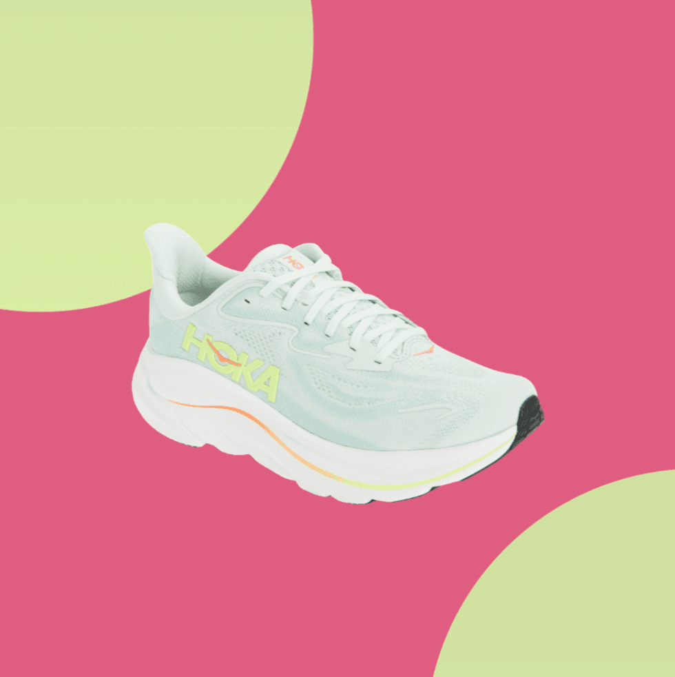 White Hoka running shoe with orange accents on pink and green background.