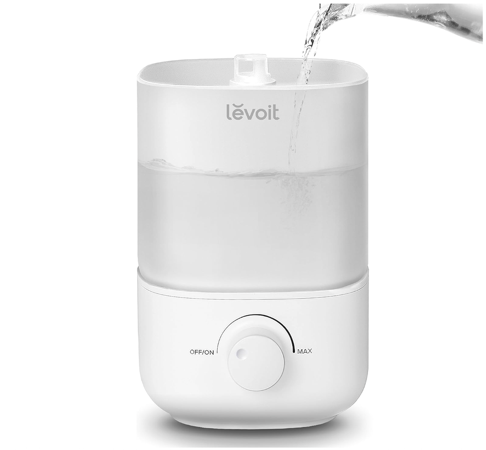 White humidifier with water being poured into the top, featuring a dial control knob.