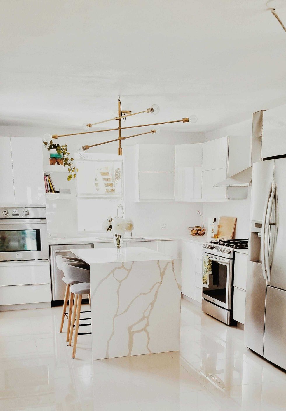 White modern kitchen with island, gold chandelier, and stainless steel appliances.