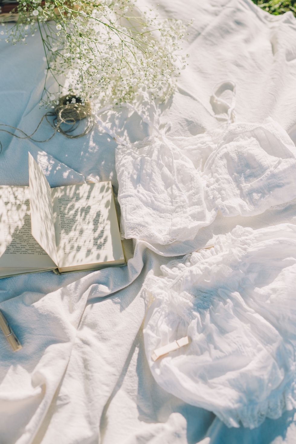 white outfit and open book pictured on a white sheet in the sunlight