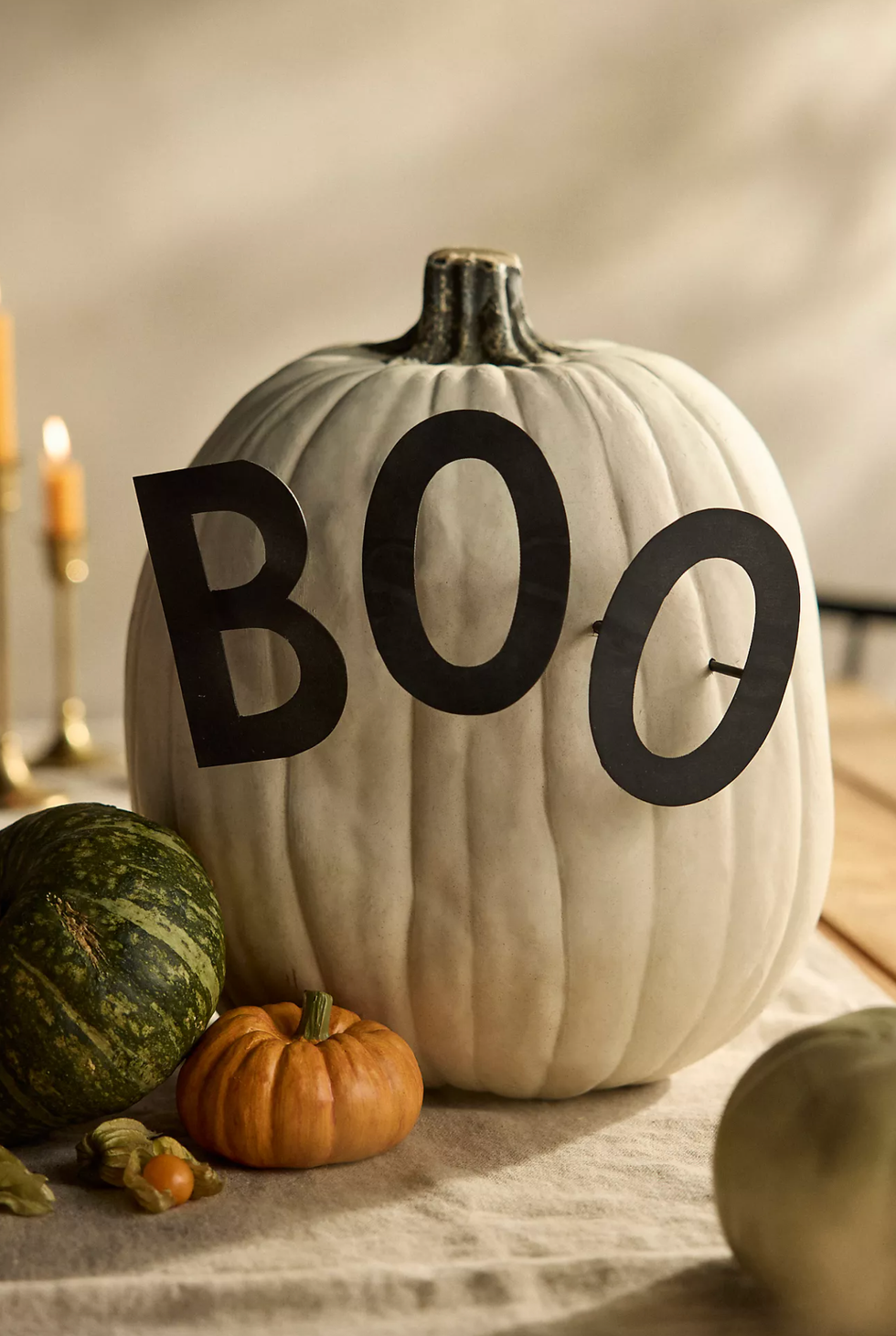 White pumpkin with "BOO" on it, surrounded by smaller pumpkins.