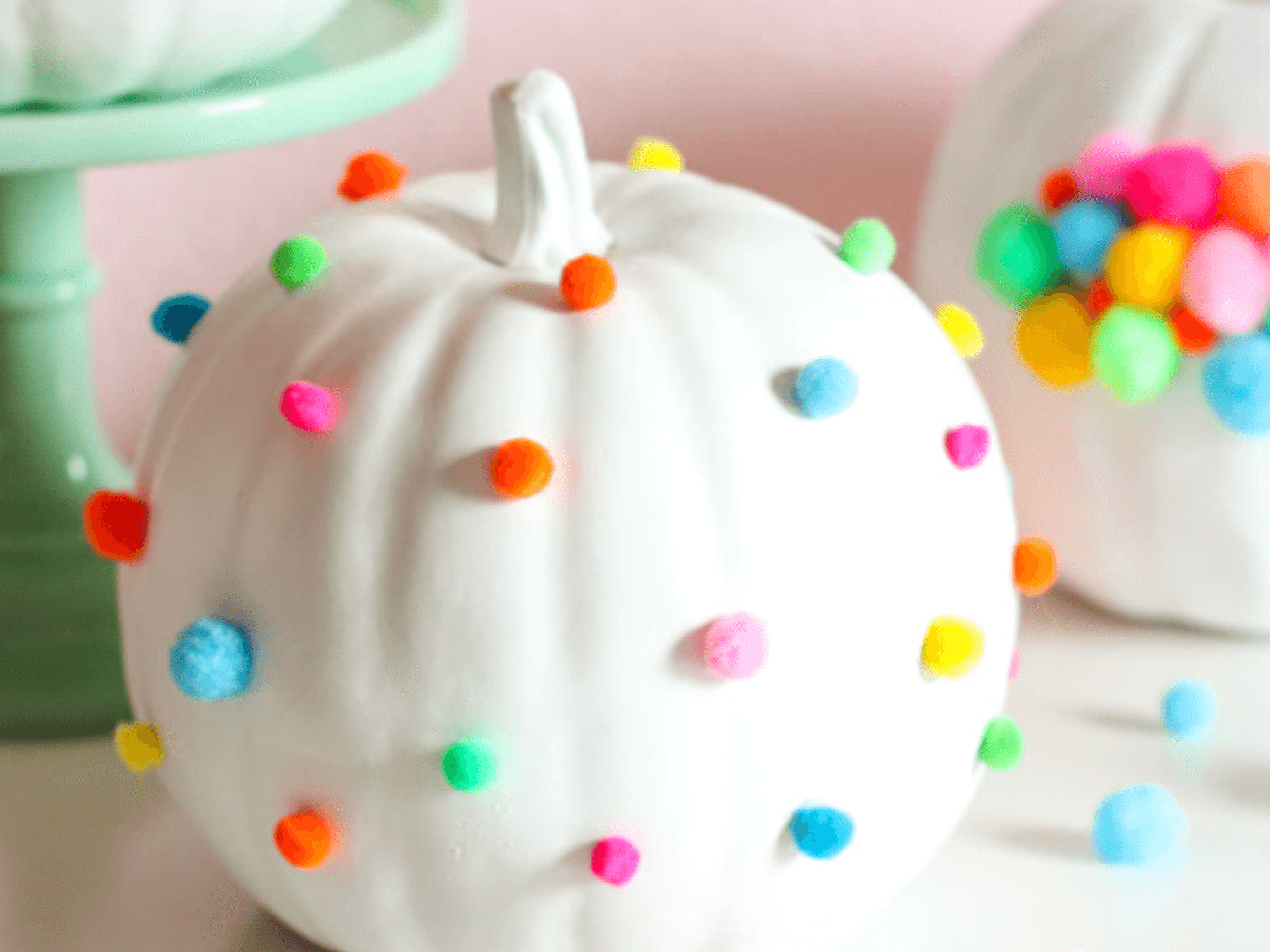 White pumpkins with colorful pom-poms on mint stand and table.