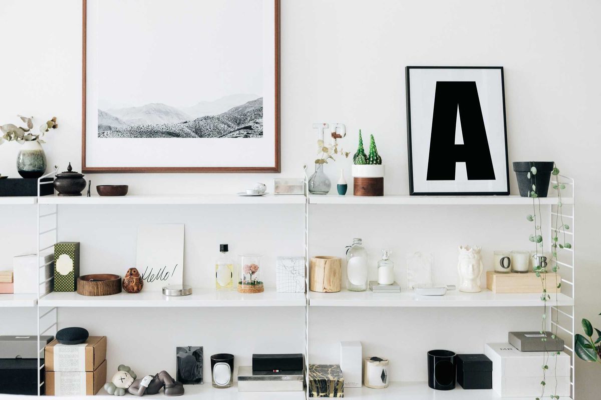 White shelf with decor, plants, and framed art on a wall. Minimalist and organized setup.