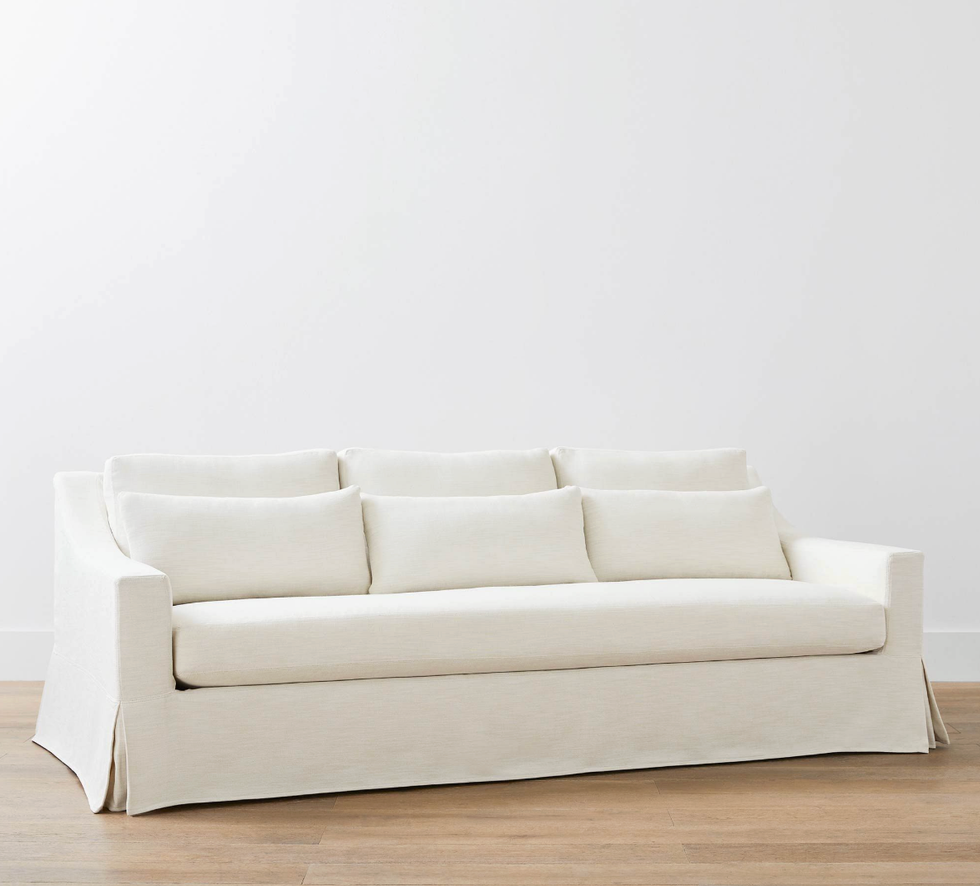 White slipcovered sofa on a wooden floor against a plain wall.