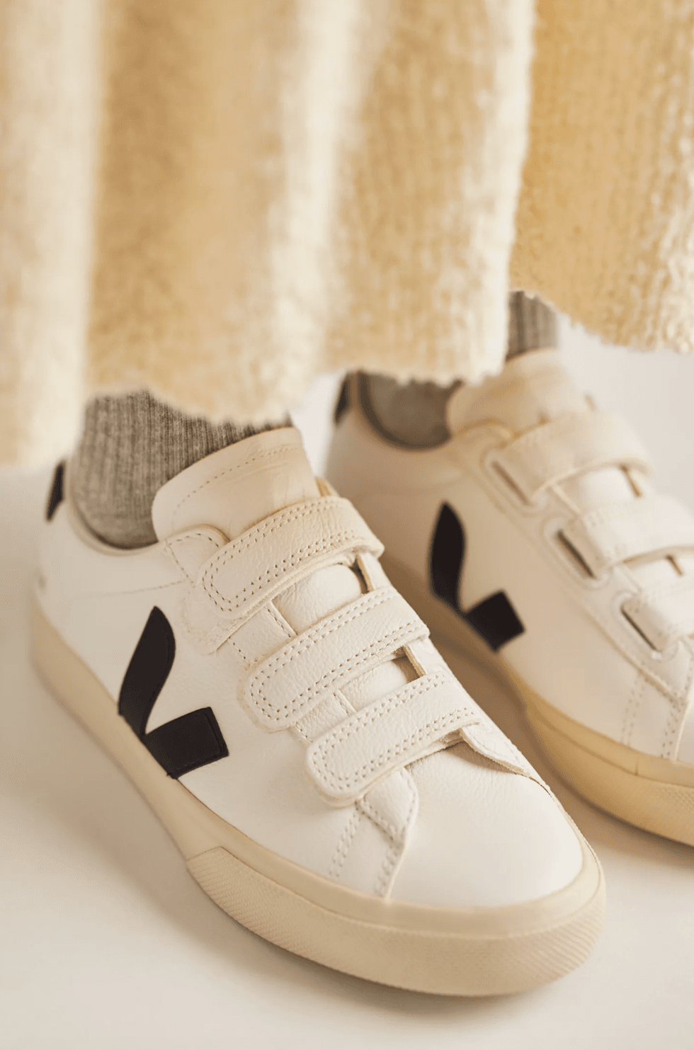 White sneakers with black logos and Velcro straps, worn with gray socks.