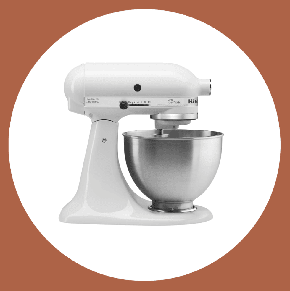 White stand mixer with stainless steel bowl on a brown and white background.