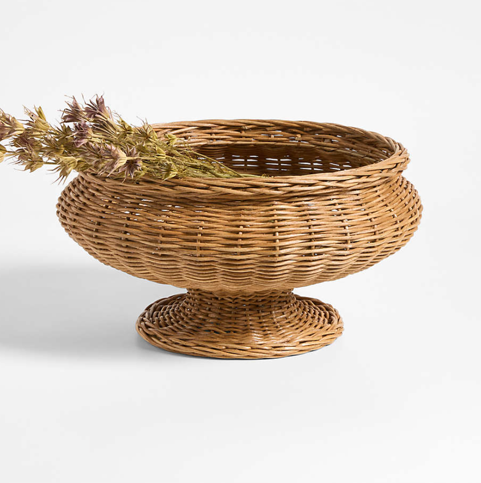 Wicker pedestal basket with dried flowers inside, set against a plain white background.