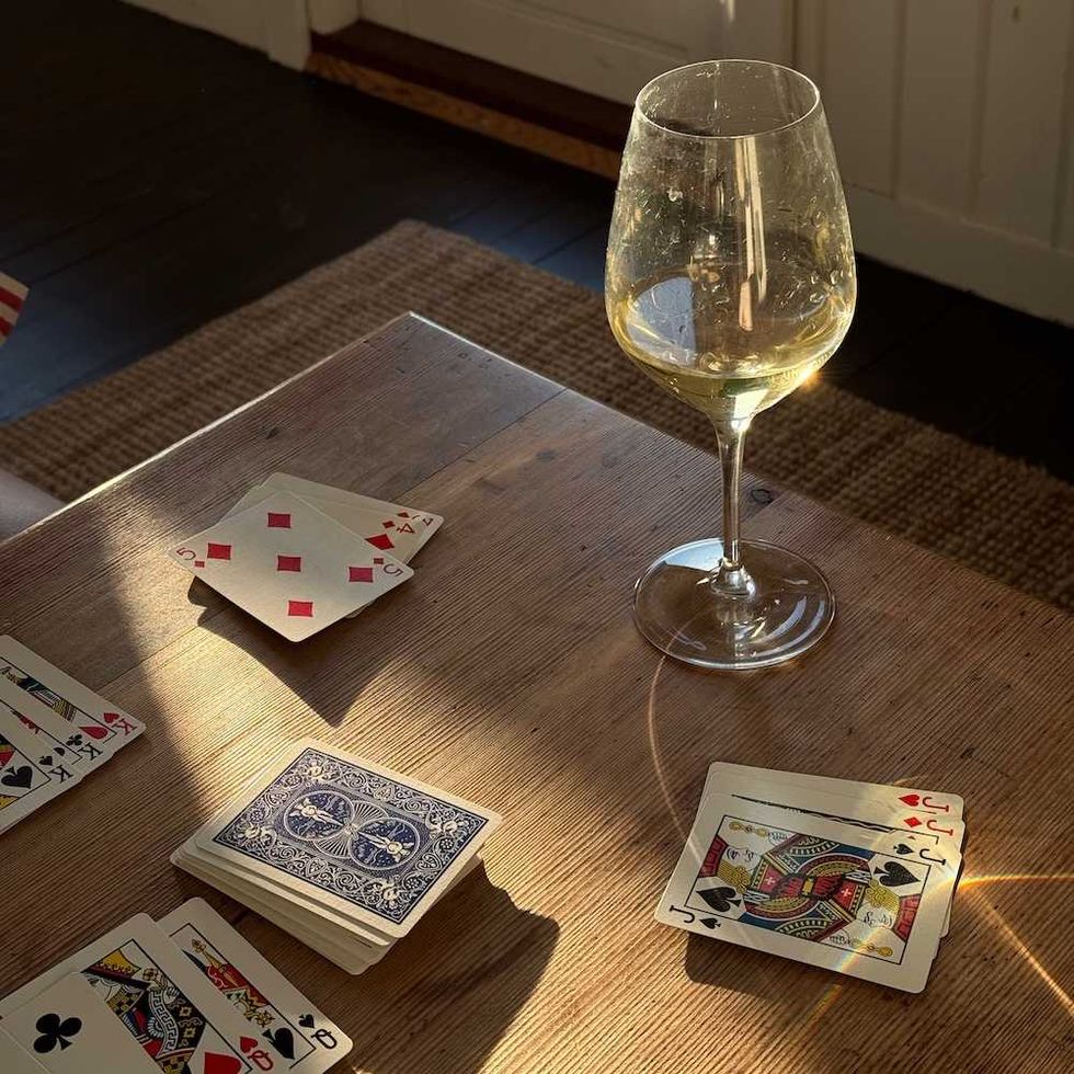 Wine glass and playing cards on sunlit wooden table.