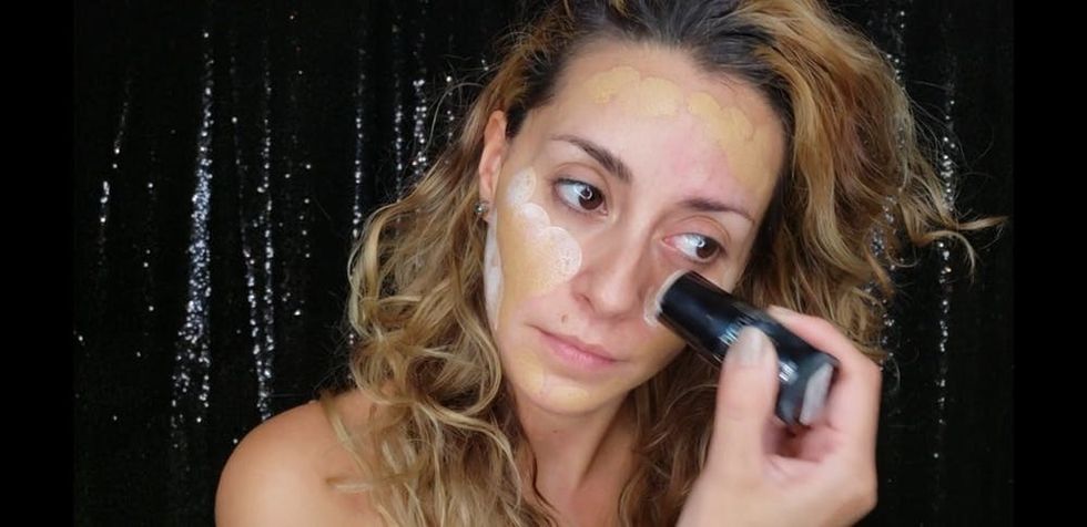 Woman applying face makeup in front of a black background.
