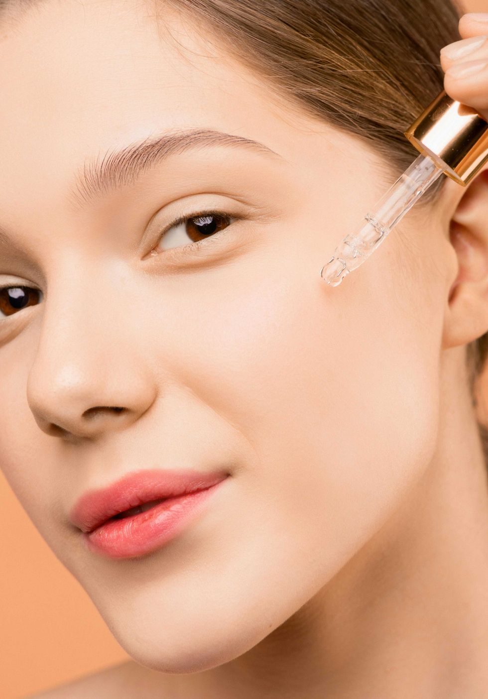 Woman applying facial serum with a dropper on her cheek.