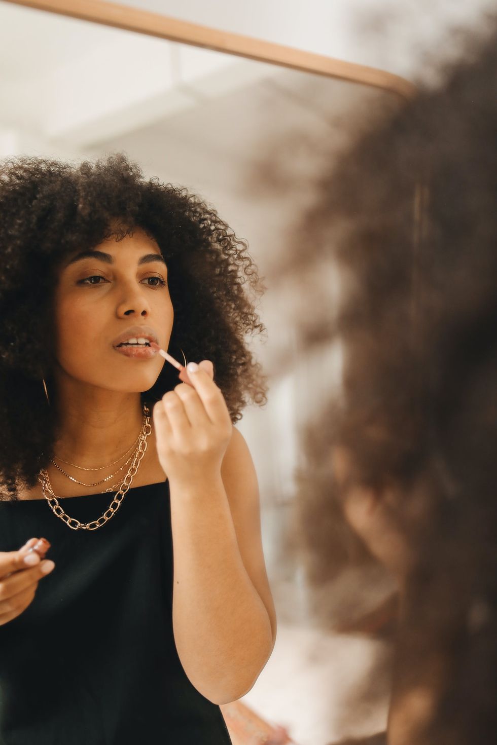 woman applying lip oil in the mirror