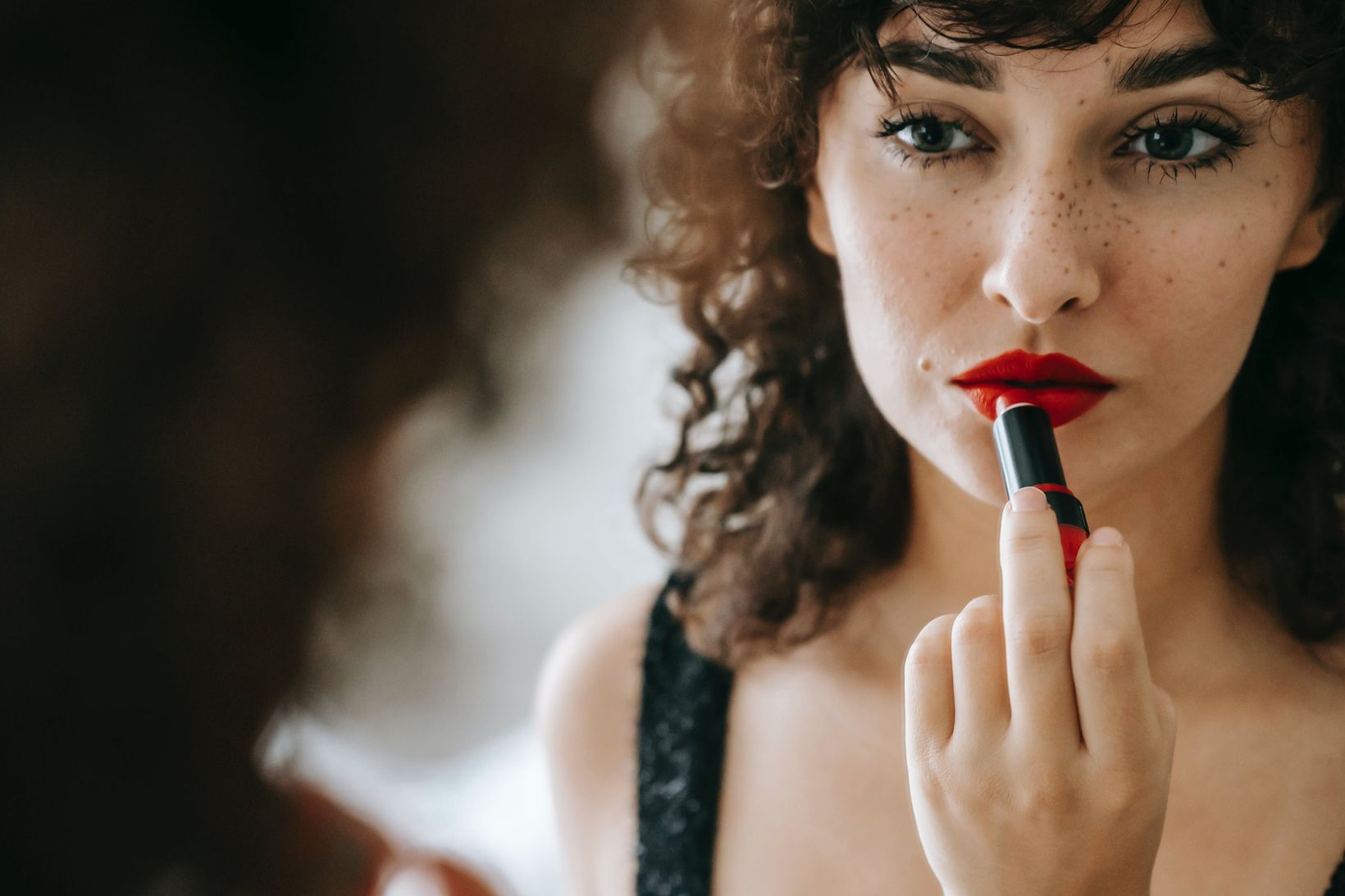 woman applying red lipstick in mirror