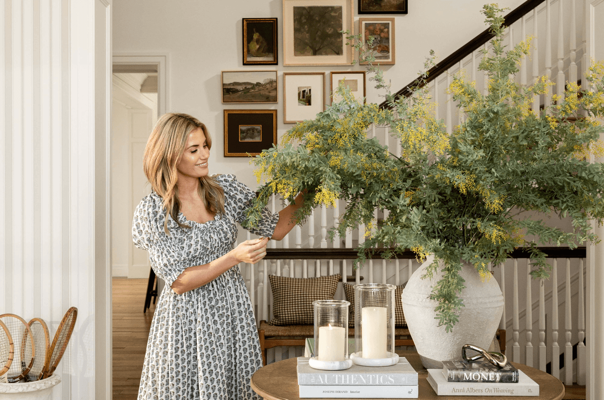 Woman arranging flowers in a vase on a table in a stylish, decorated room.