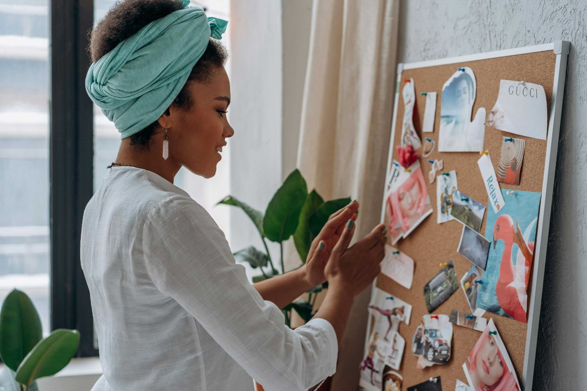 Woman arranging pictures on a vision board in a light-filled room.