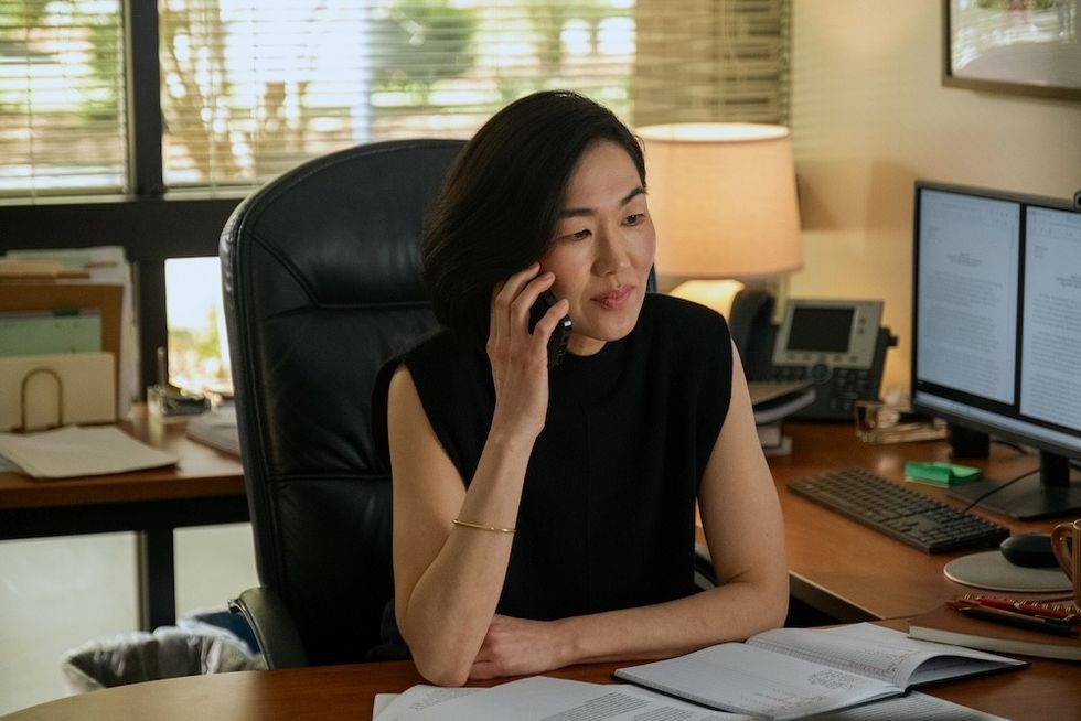 Woman at desk talking on phone, papers and dual monitors in the background.