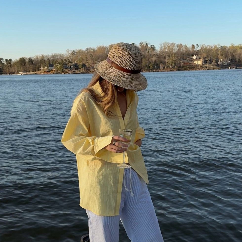 woman by the water with a straw hat and a glass of wine