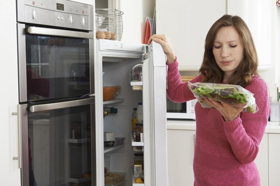 Woman checking sell-by date on produce in refrigerator
