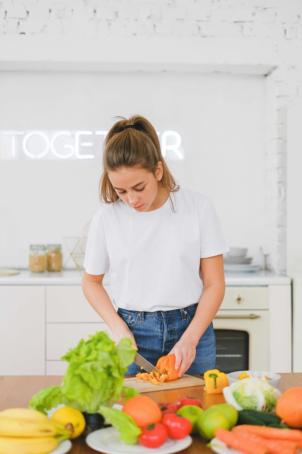 Woman chopping vegetables in a bright kitchen with fresh produce on the table.