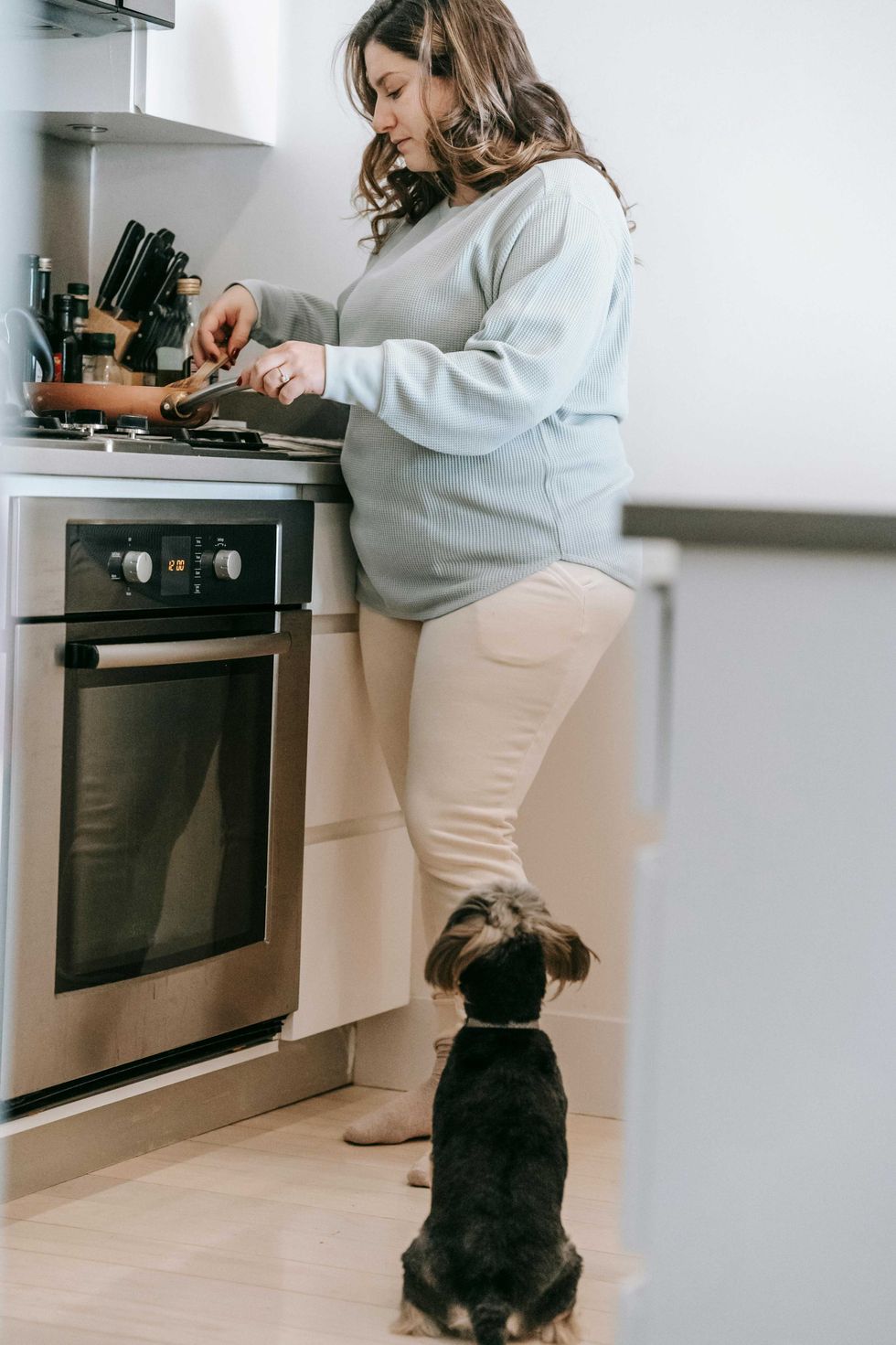 Woman cooking at a stove, with a small dog sitting by her feet.