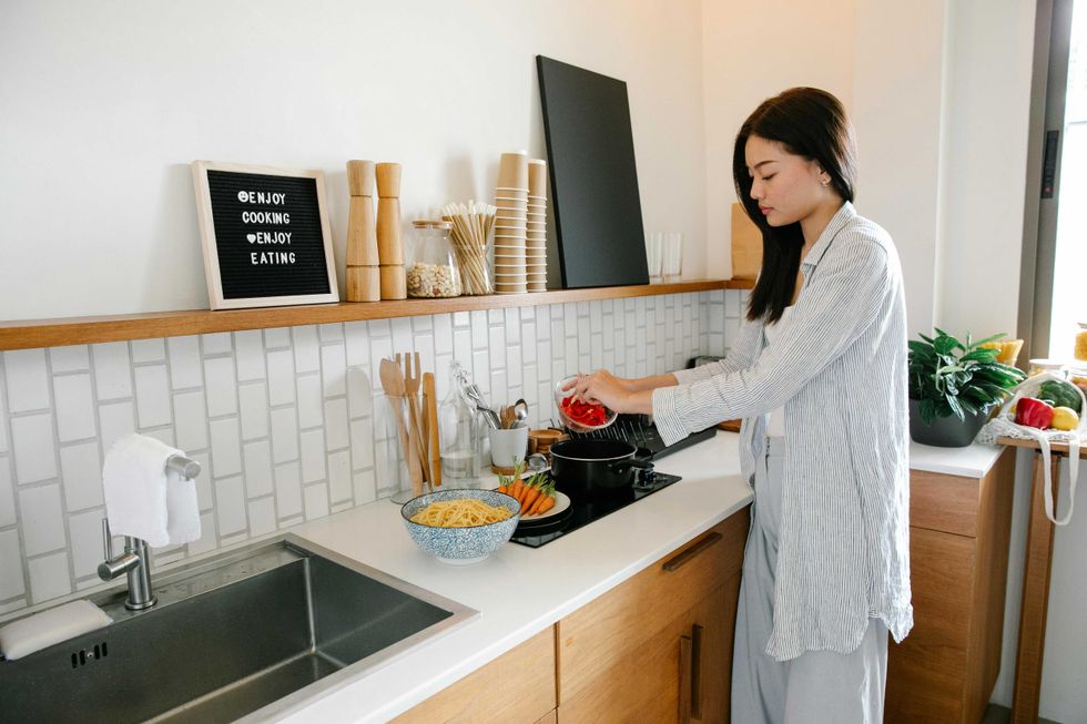 Woman cooking in a kitchen, adding ingredients to a pan on the stove.