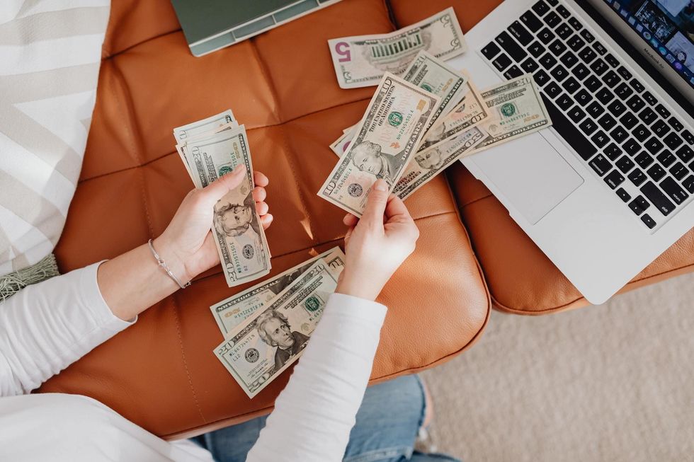 woman counting money dollar bills at computer on couch