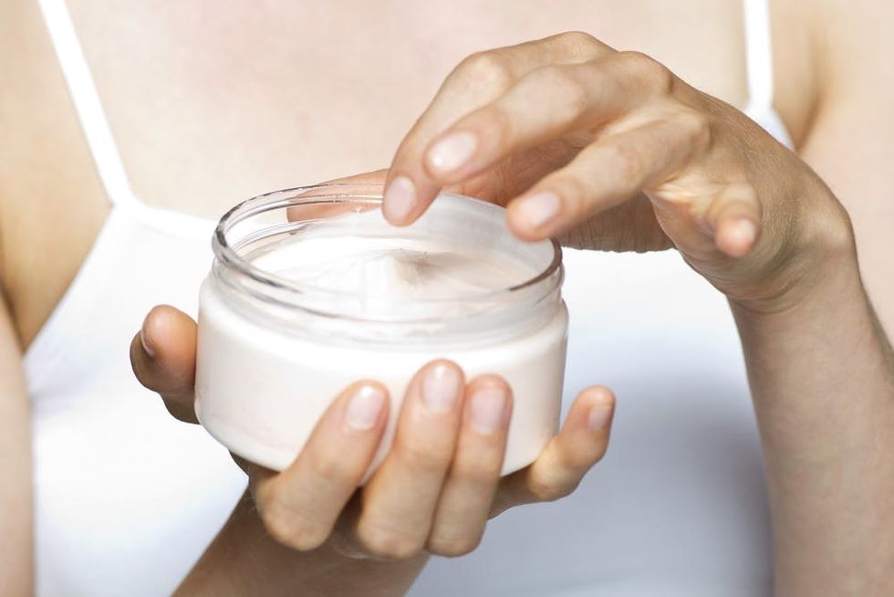 Woman dipping fingers into jar of moisturizer.