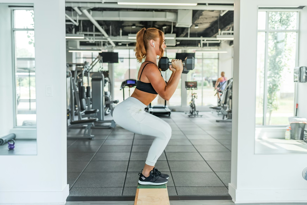 Woman doing squats with dumbbells on a platform in a modern gym.