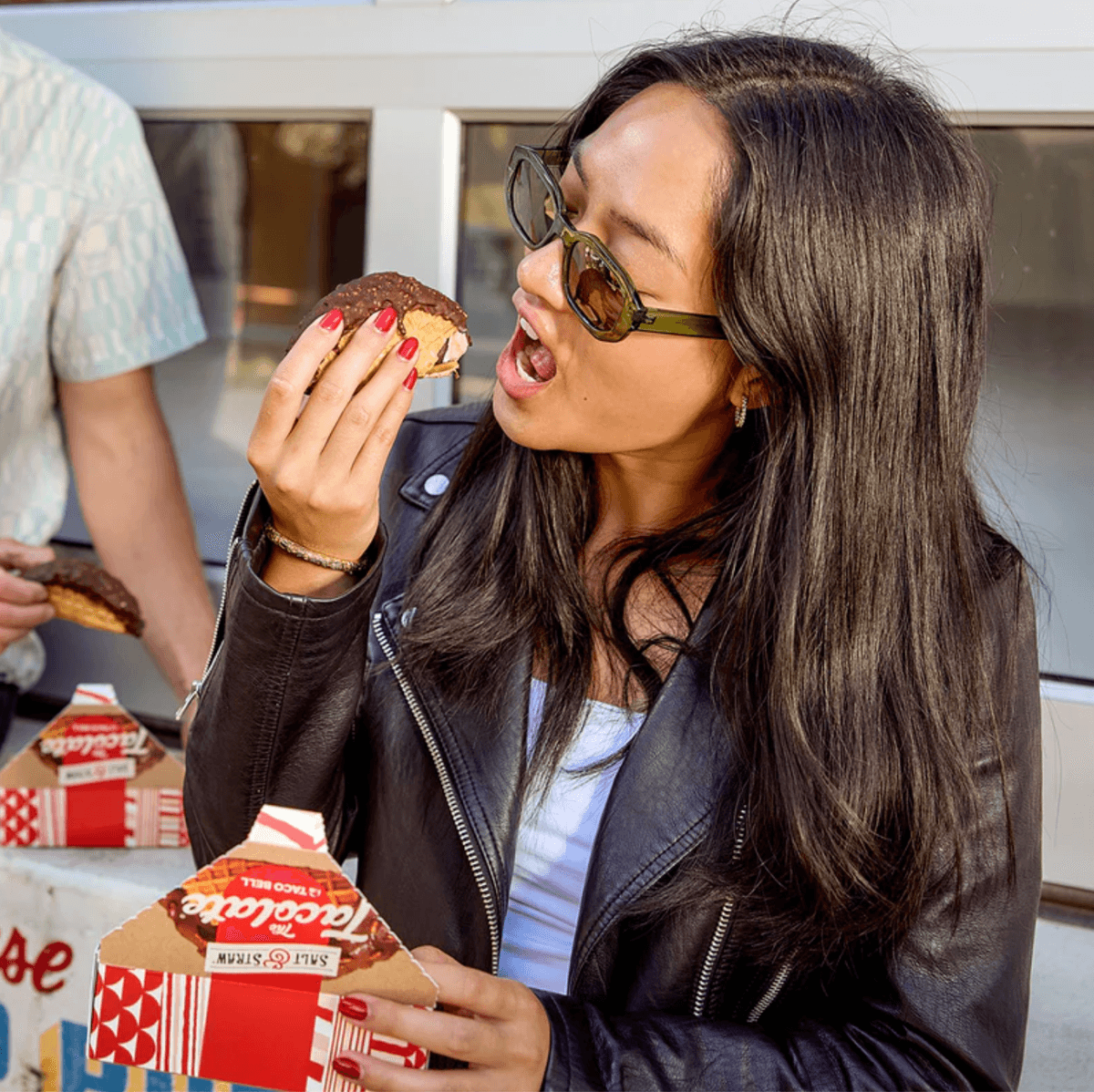 Woman enjoying an ice cream taco outside, holding a package.