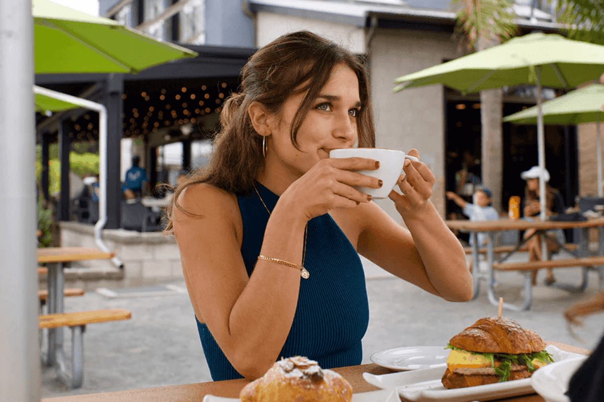 Woman enjoying coffee and pastries at an outdoor cafe with green umbrellas.