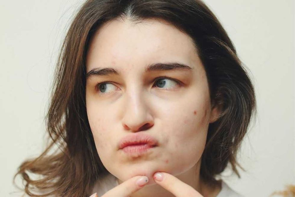 Woman examining chin acne with a thoughtful expression.