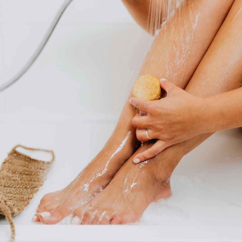 woman exfoliating her legs in the bath